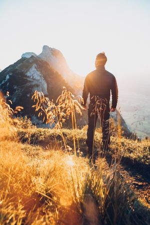 Back view silhouette of a man standing on brown grass facing the sun