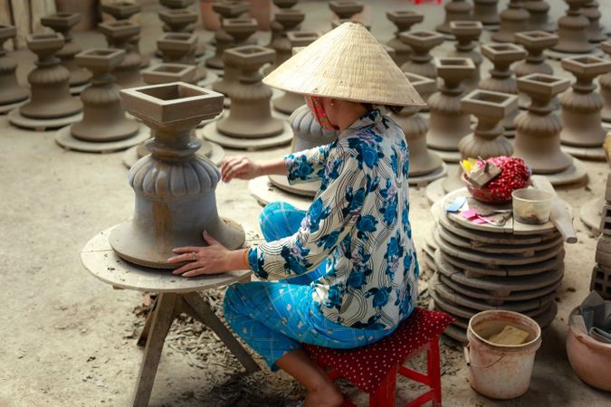 Back view of woman with conical hat making pottery