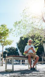 Vertical shot of mature man sitting outdoor on a bench using a phone 4AgAq0