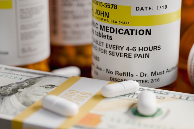 Prescription Medicine Bottles and Pills Next To Stacks of 100 Dollar Bills.