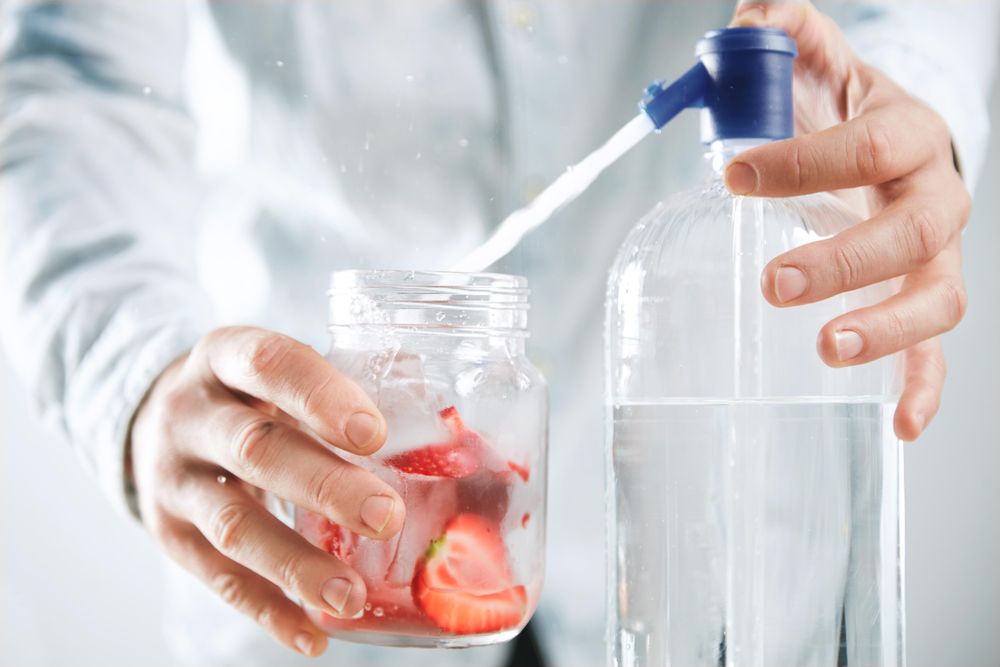 Man filling mason jar filled with strawberry with water to make flavored drink