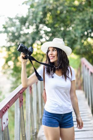 Woman walking with SLR camera, wearing straw hat outside, vertical