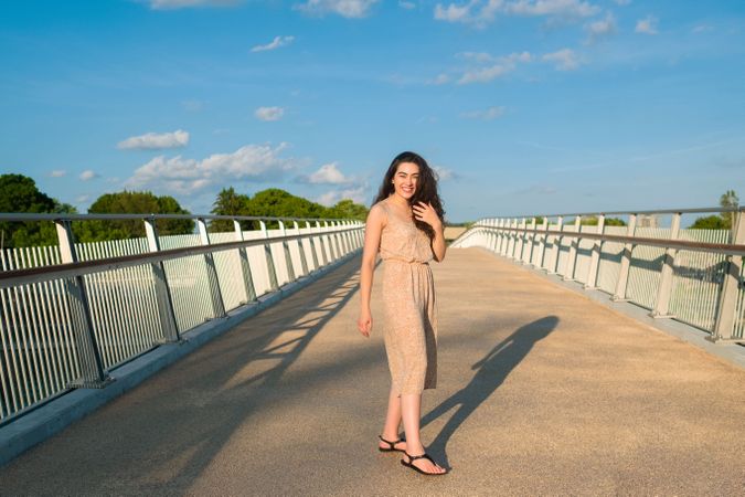 Peaceful woman in dress walking along rural bridge