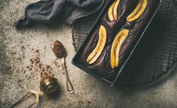 Freshly baked dark chocolate banana bread cake on concrete counter, with cocoa powder