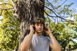 Handsome young man leaning on a tree while listening to music