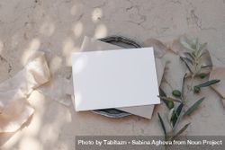 Blank greeting card, envelope on silver plate with olive tree branches on beige marble background 5RVPoD