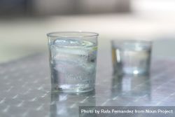 Two glasses of water with ice on a metallic table outdoors 0JGP6w