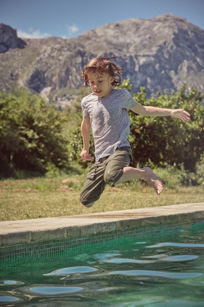 Cute kid jumping into water of swimming pool
