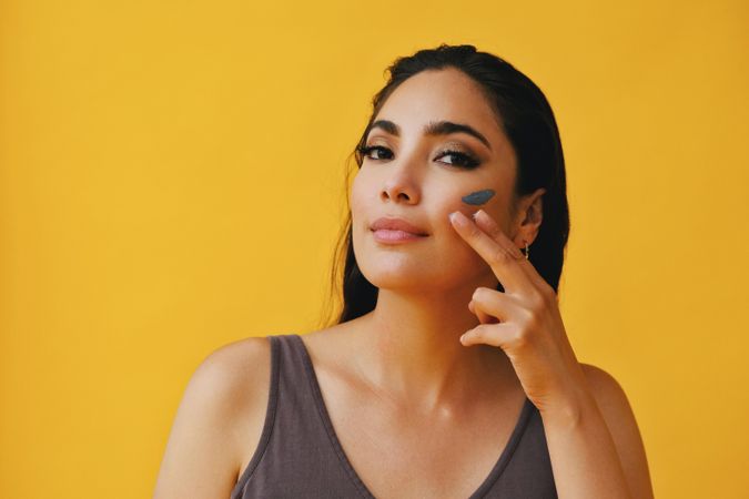 Latina woman applying clay mask with hand