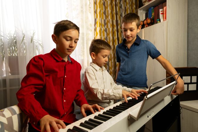 Three boys playing the piano together in cozy home setting.