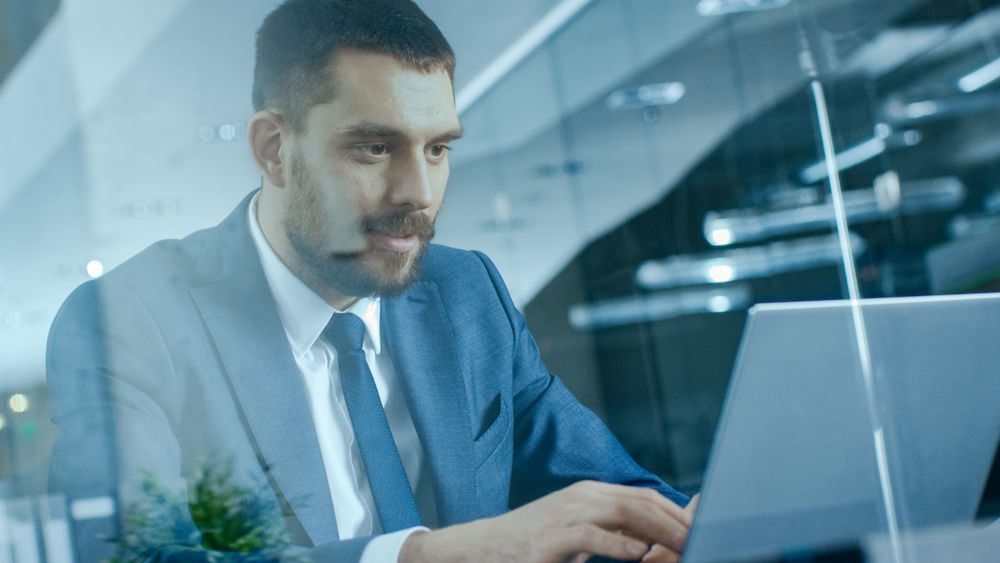 Confident Businessman Works on a Laptop at His Desk