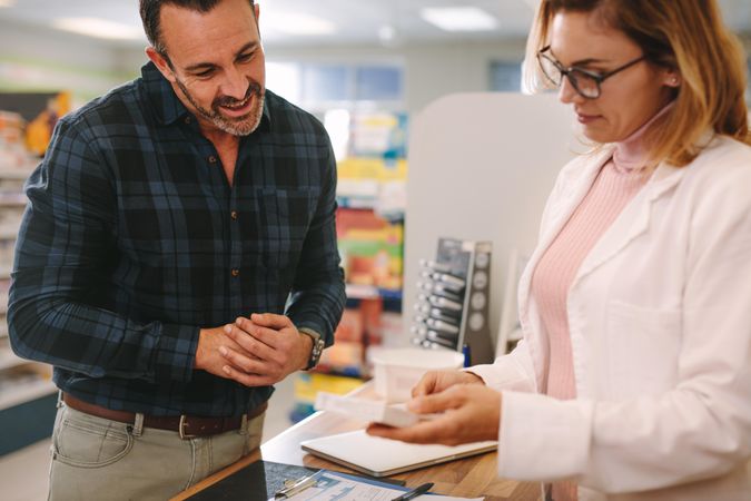 Female pharmacist holding medicine box giving advice to customer in chemist shop