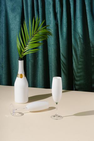 Champagne with palm leaf and glassware in front of green curtain background