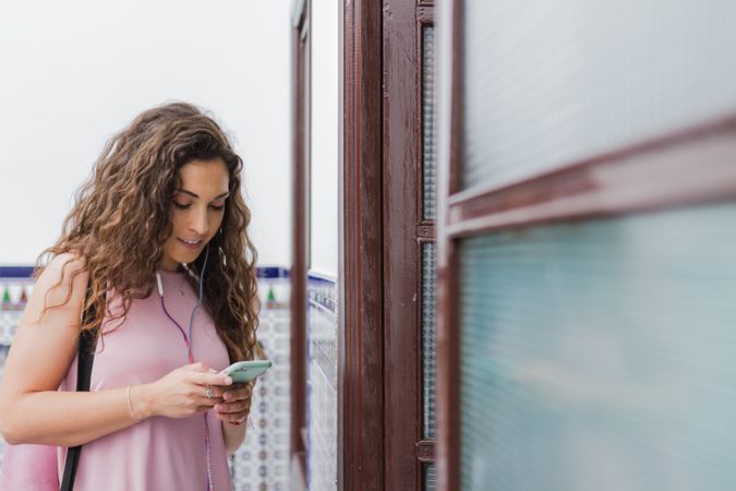 Woman with smartphone and headset beside entrance