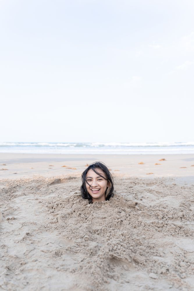 A young Hispanic woman is having fun while buried in the sand of the beach