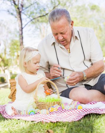 Grandfather and Granddaughter Coloring Easter Eggs on Blanket At Park