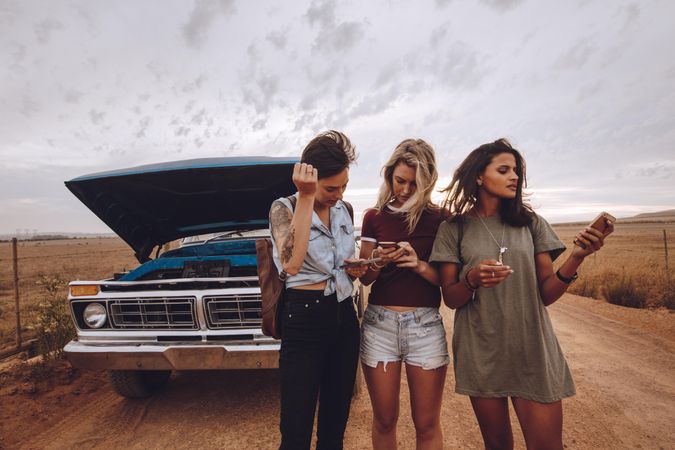 Three female friends making a phone call after their car break down on country road