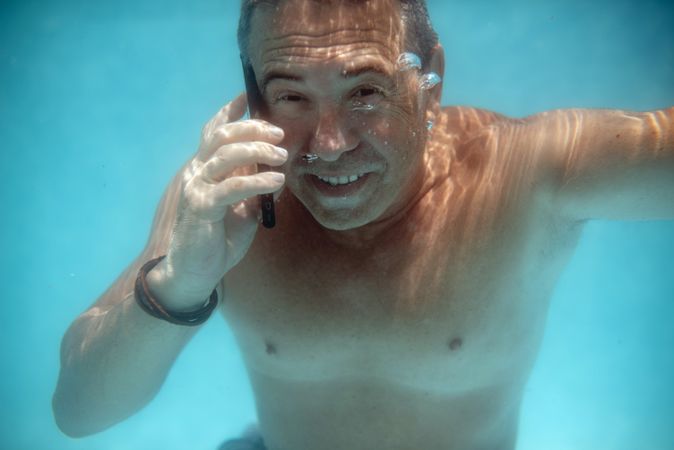 Mature man diving under water with smartphone