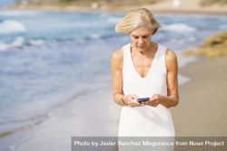 Older woman using her phone on a rocky beach 47o2k4