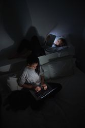 Woman and boy surfing gadgets in dark room at home