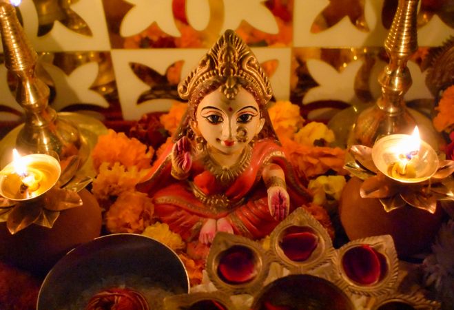 Small statue of Lakshmi Hindu Goddess surrounded by diya and flowers