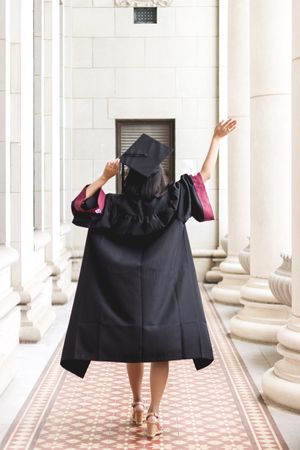 Woman walking in hallway wearing mortarboard and academic gown