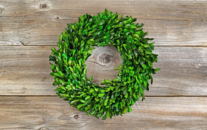 Wreath made of green boxwood leaves on rustic wood