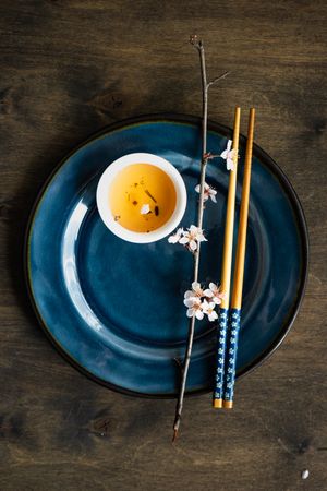 Top view of table setting with chop sticks on ceramic navy plate and delicate cherry blossom branch and green tea