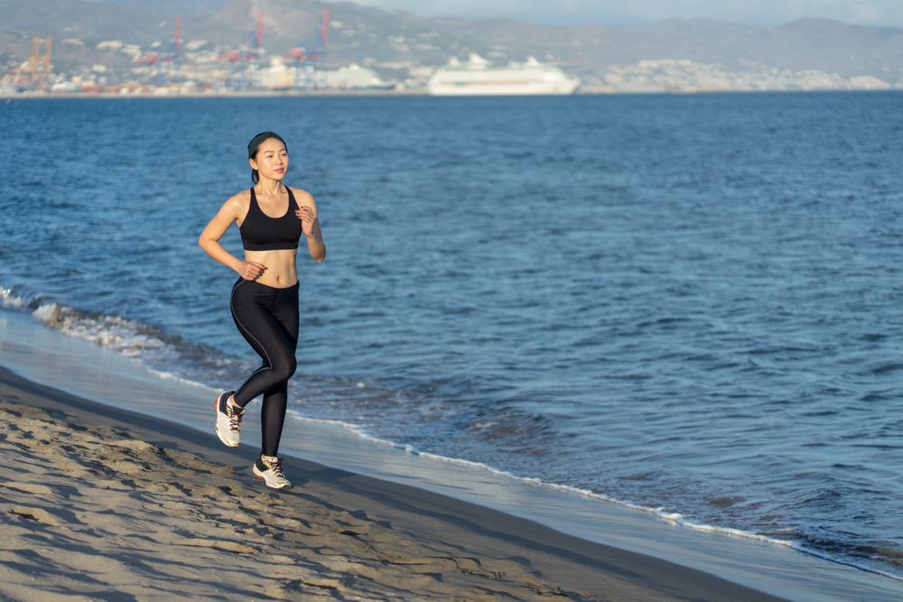 Sportswoman running on sandy sea beach on sunny day