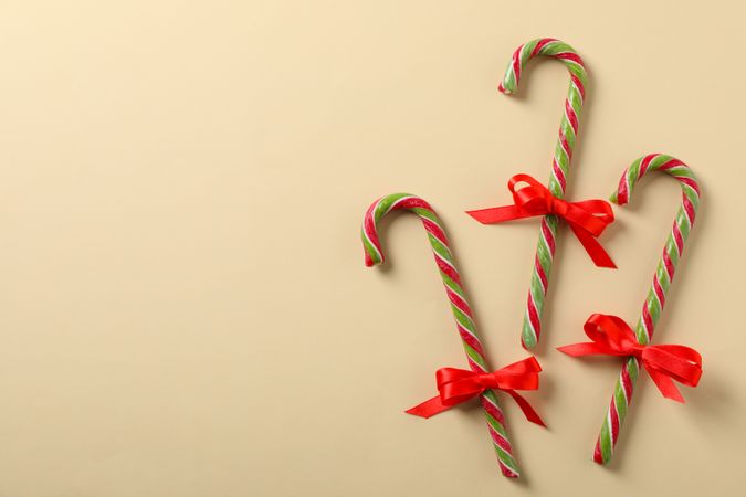 Sweet candy canes with bow on color background, space for text