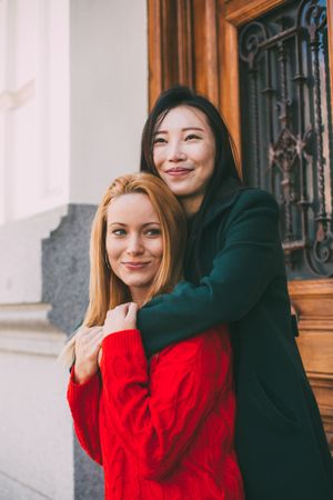 Cheerful female friends hugging near ornamental door