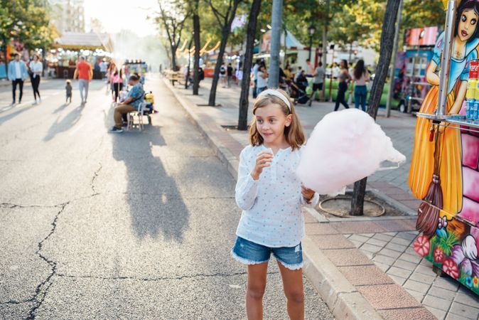 Cheerful girl eating cotton candy on street
