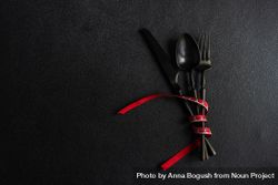 Dark cutlery on dark background tied with bright red ribbon 0LxnA0