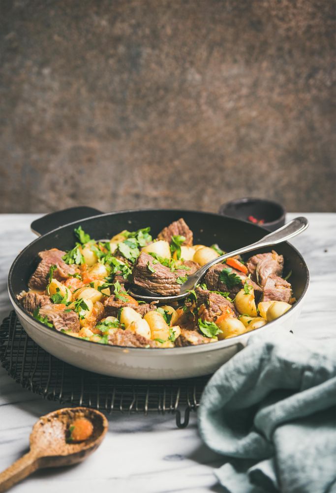 Braised beef stew with potatoes, carrots and parsley, with wooden spoon, copy space