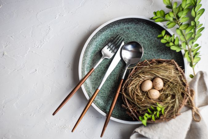 Top view of Easter table setting with nest and mini eggs, on blue plate with silverware