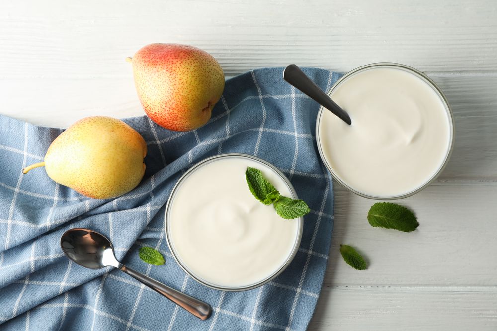 Cream yogurt, pears, towel and mint on wooden background, space for text