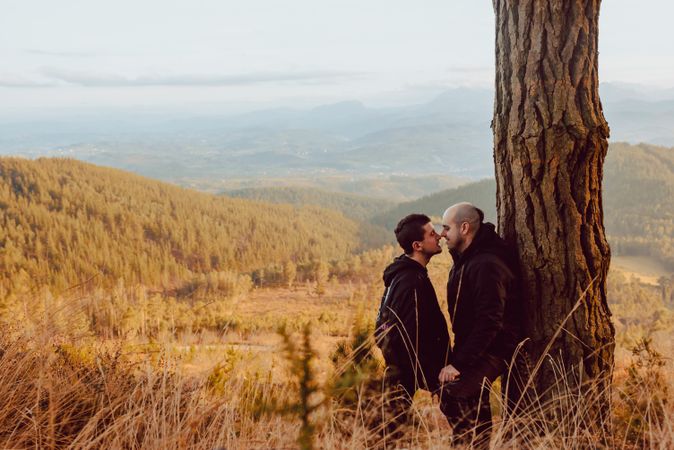 Smiling men hugging near tree in forest on hill