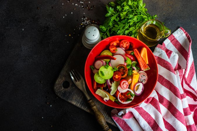Colorful healthy raw vegetable salad served in red bowl with red striped napkin