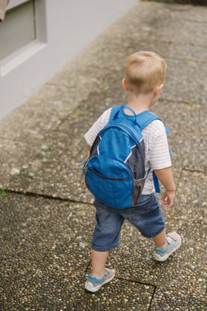Adorable unrecognizable child with backpack walking on side road