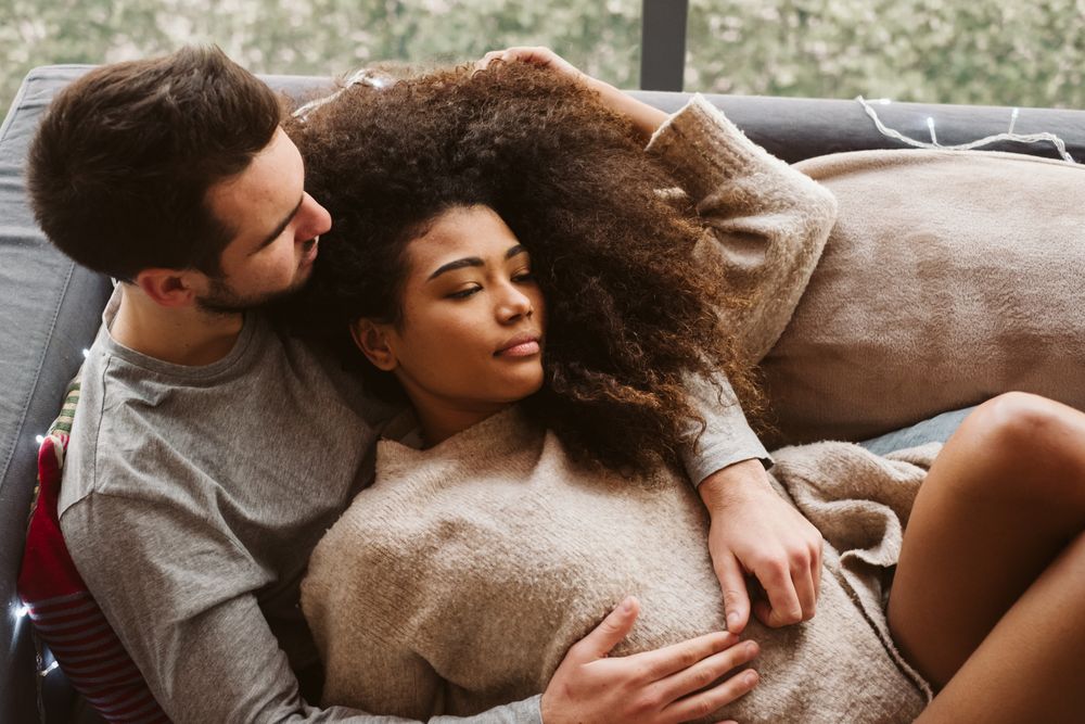 Young multiracial couple hugging on sofa