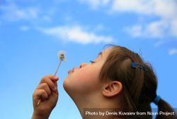 Young child blowing dandelion flower with blue cloudy sky in the background 5w96Zb