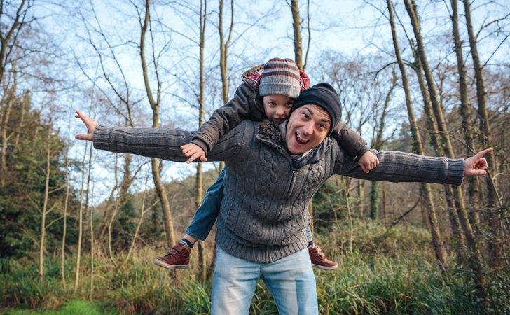 Father giving son ride on his shoulders in forest with arms outstretched