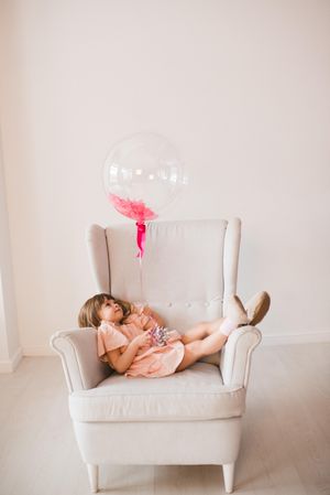 Girl in pink dress holding a balloon lying on gray armchair