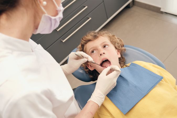 Unrecognizable dentist examining teeth of boy