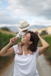 Adorable kid in hat on shoulders and looking at mother