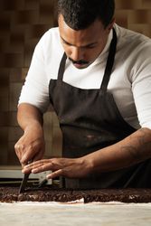 Black male in apron looking down focused on slicing brownies