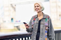 Joyful blonde female listening to music on phone along river walk