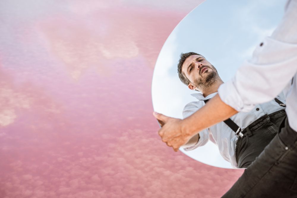 Stylish man holding mirror with reflection