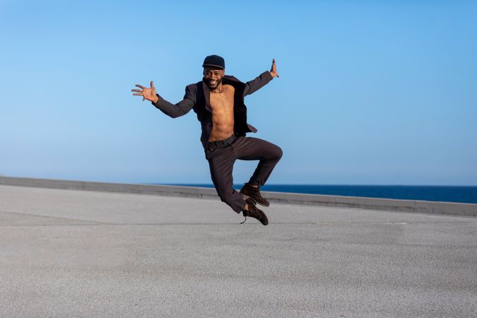 Smiling Black man jumping high and clicking heels with open shirt outside