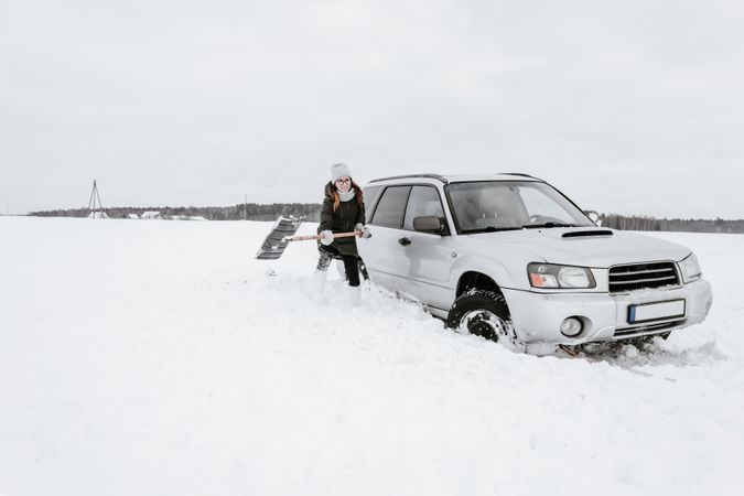 Woman with shovel near car on snow field